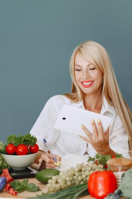 Woman using a tablet surrounded by fresh vegetables at a table, showcasing healthy lifestyle and technology.
