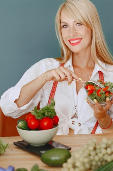 Blonde woman enjoying a fresh salad surrounded by vegetables, promoting healthy eating.